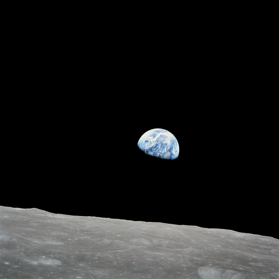 Earth, half lit, rising over the grey horizon of the Moon.